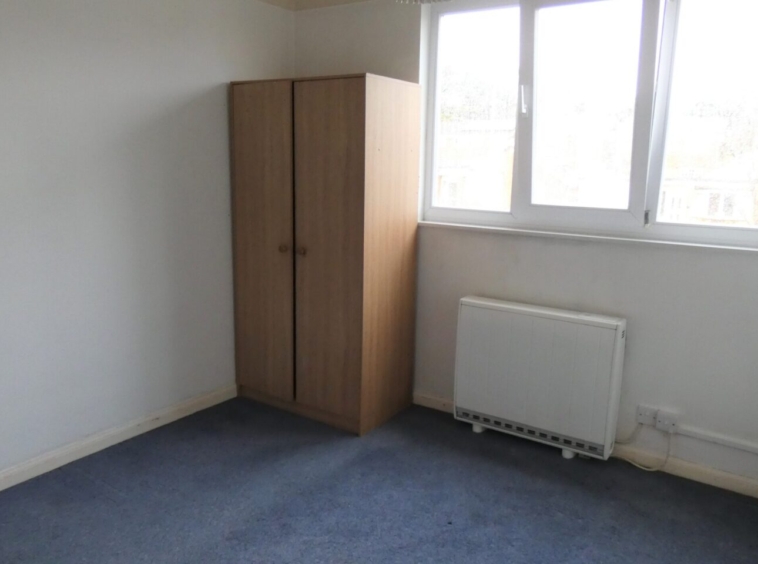 A bedroom with blue carpet, white walls and a wooden wardrobe