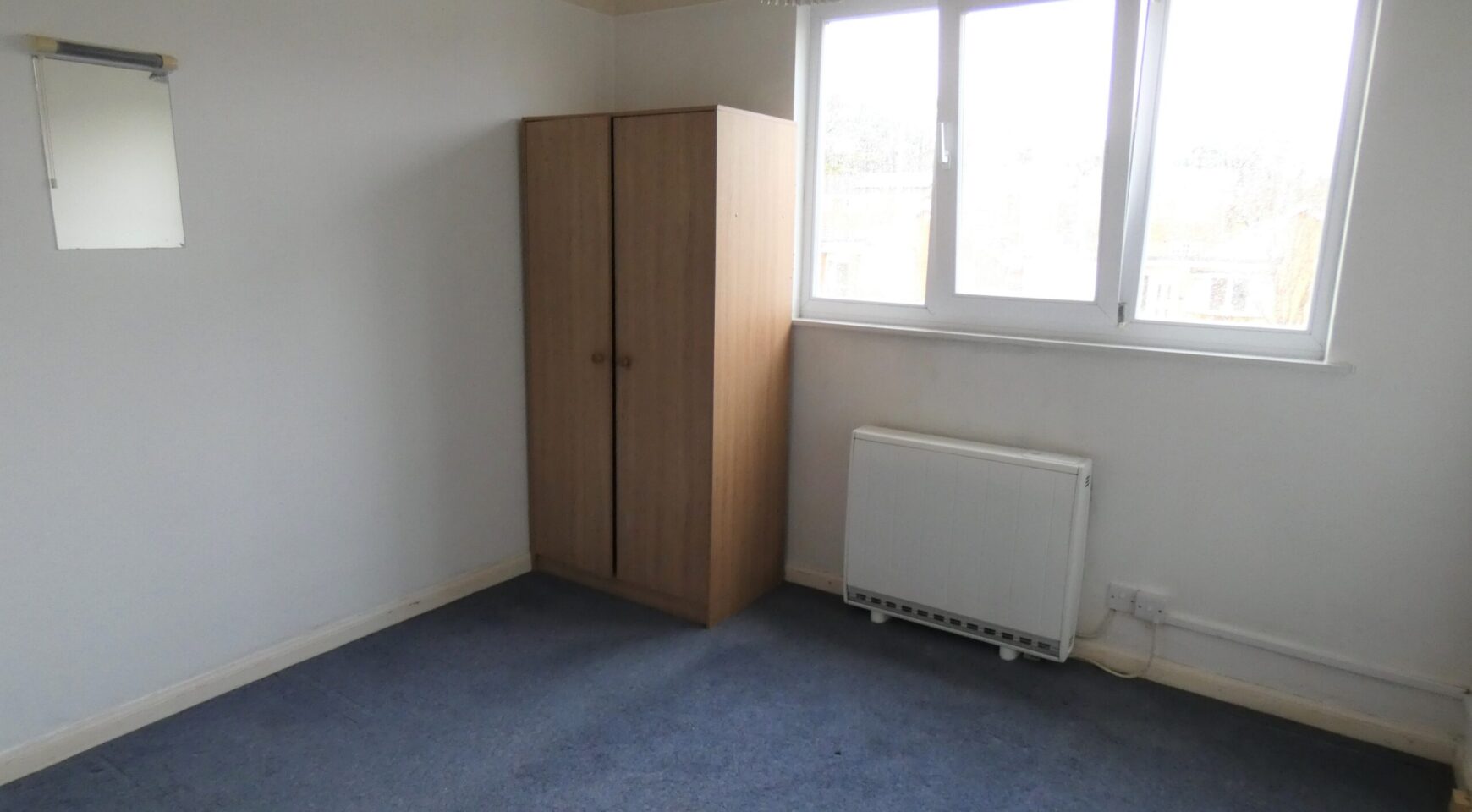 A bedroom with blue carpet, white walls and a wooden wardrobe