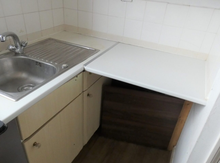 A kitchen with sink, wooden cabinets and white worktops
